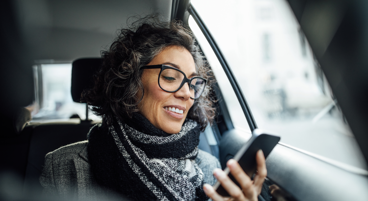 middle aged woman with glasses looks at a smart phone while riding in a car