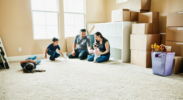 Family in unfurnished living room with cardboard boxes behind them