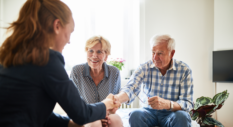 business woman shaking hands with an elderly couple sitting in a living room